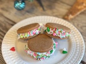 Festive gingerbread sandwich cookies with Pillsbury frosting and colorful holiday sprinkles on a white plate.