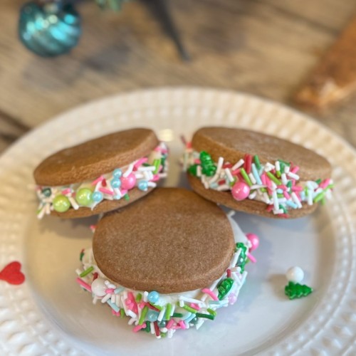 Festive gingerbread sandwich cookies with Pillsbury frosting and colorful holiday sprinkles on a white plate.