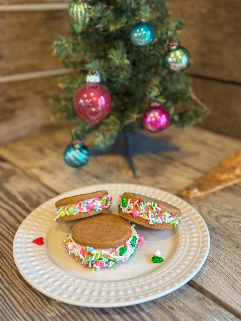 Festive gingerbread sandwich cookies with Pillsbury frosting and colorful holiday sprinkles on a white plate.