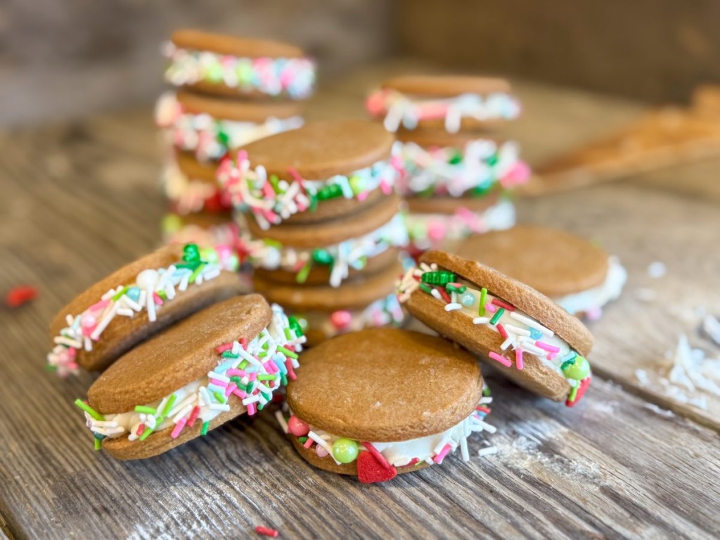 Close-up of gingerbread sandwich cookies made with Pillsbury gingerbread dough, filled with creamy vanilla frosting, and rolled in vibrant holiday sprinkles, displayed on a rustic wooden surface.