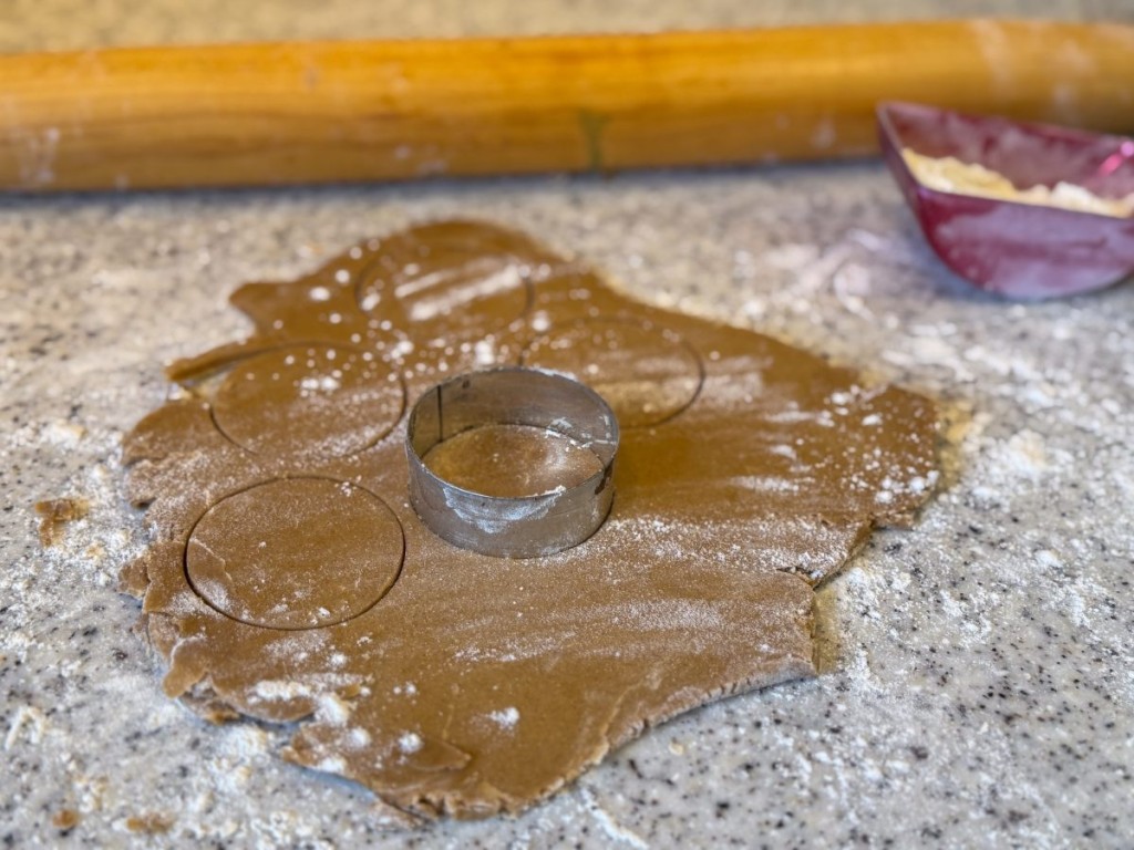 Gingerbread cookie dough rolled out on a floured surface with a circle cookie cutter, ready for baking festive sandwich cookies made with Pillsbury dough and perfect for holiday treats.