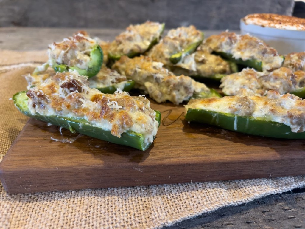 Sausage and cheese stuffed jalapeños baked to a golden finish, served on a wooden board with a spicy dipping sauce, perfect for an easy, crowd-pleasing appetizer.