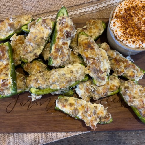 Sausage and cheese stuffed jalapeños baked to a golden finish, served on a wooden board with a spicy dipping sauce, perfect for an easy, crowd-pleasing appetizer.