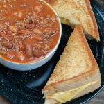 A bowl of thick and hearty bar chili served with a classic grilled cheese sandwich on a rustic wooden table, showcasing comfort food perfect for chilly days or game day gatherings.