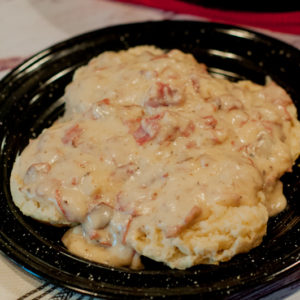 Plate of creamy dried beef gravy served over feshly baked biscuits on a white barnwood table.