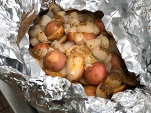Cooked red potatoes and sliced onions inside an open foil packet, seasoned with black pepper and steaming hot from the grill.