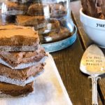 Stack of homemade brownies with sugar edges on a wooden table, featuring decorative kitchen items like a glass dome full of brownies and a dessert spoon with the inscription 'I'm just here for dessert', food and lifestyle blogging at farmwifefeeds.com
