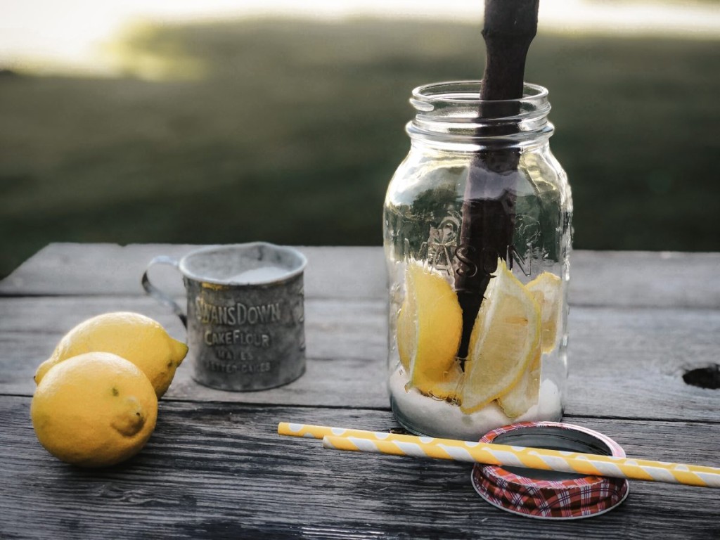 ball jar with water sugar and lemons, whole lemons and paper straws