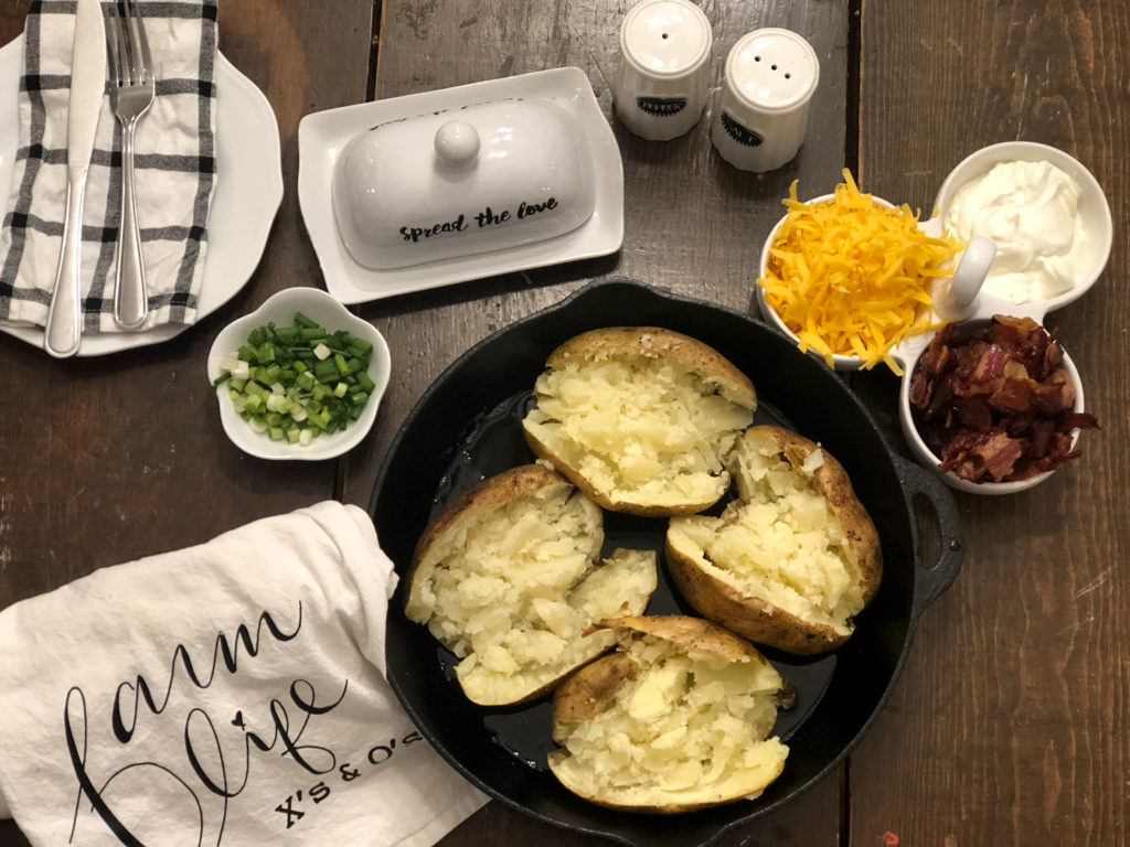 4 baked potatoes in cast iron skillet on a table with shredded cheese