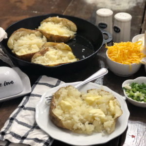 cast iron skillet with baked potatoes plate with baked potato on table