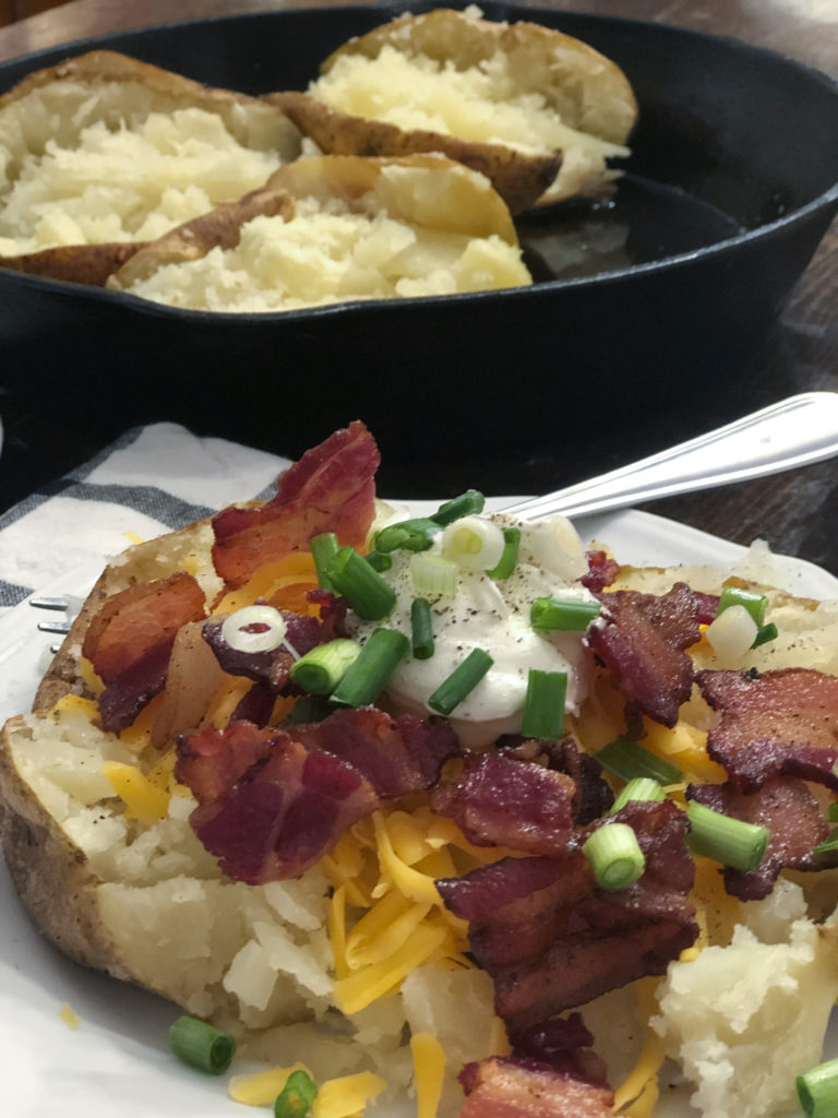 baked potato on plate with bacon green onions, cheese
