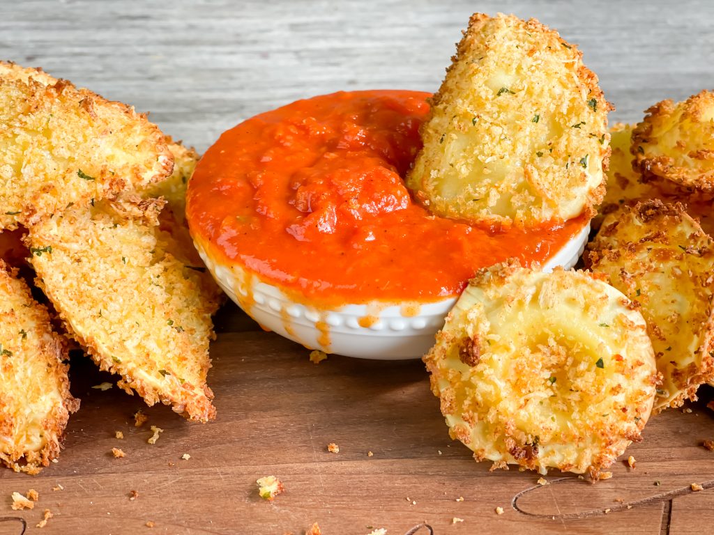 picture of crispy ravioli that has been air fryed with small bowl of marinara for dipping words