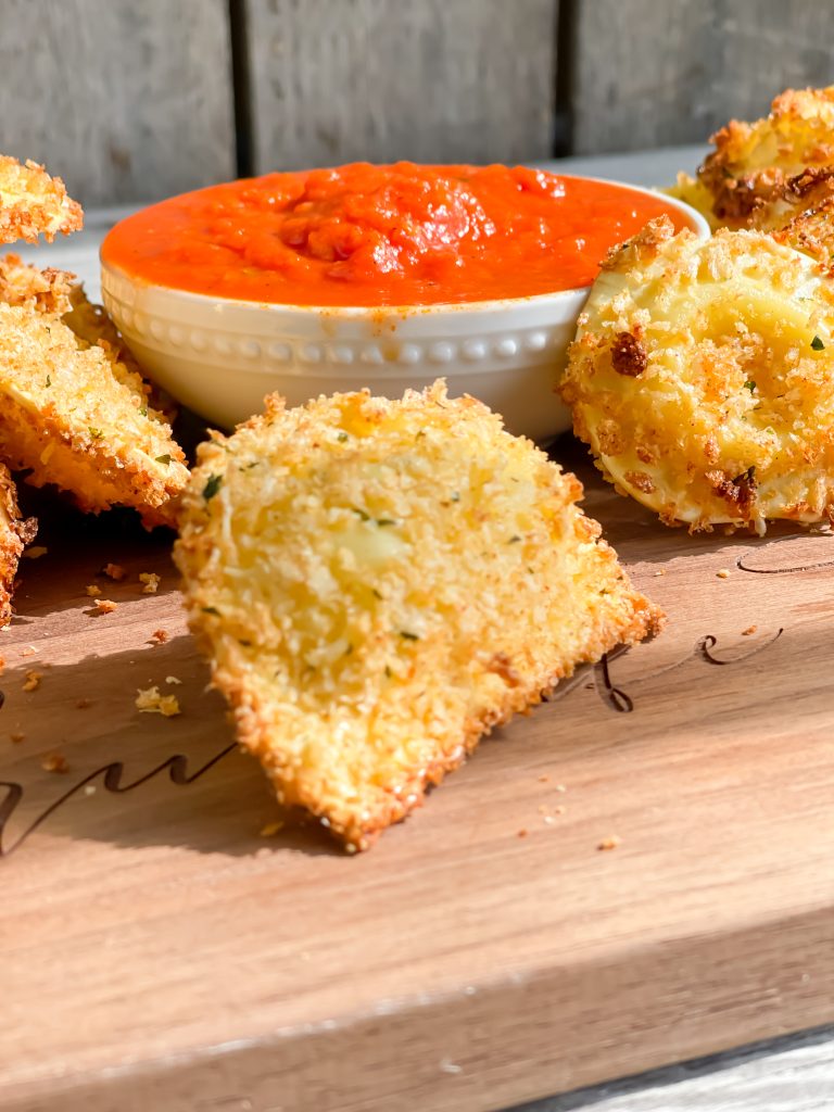 picture of crispy ravioli that has been air fryed with small bowl of marinara for dipping words