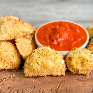 picture of crispy ravioli that has been air fryed with small bowl of marinara for dipping words