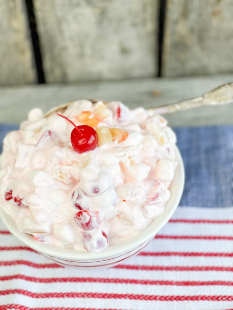 white creamy fruit salad in a bowl with a red cherry on top