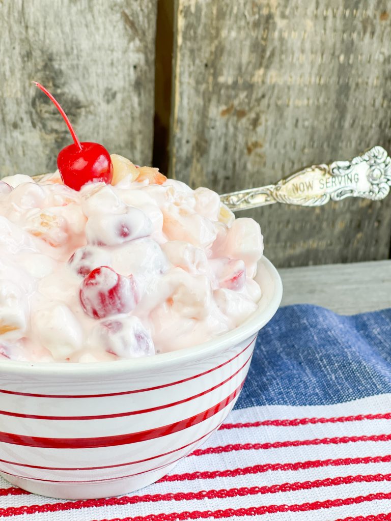 white creamy fruit salad in a bowl with a red cherry on top