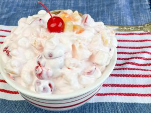 white creamy fruit salad in a bowl with a red cherry on top