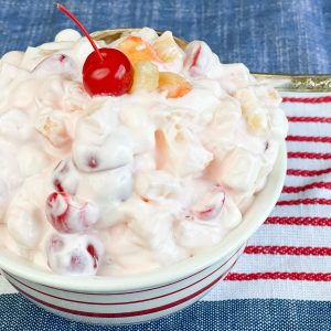 white creamy fruit salad in a bowl with a red cherry on top