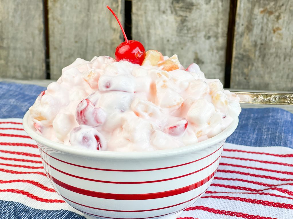 white creamy fruit salad in a bowl with a red cherry on top