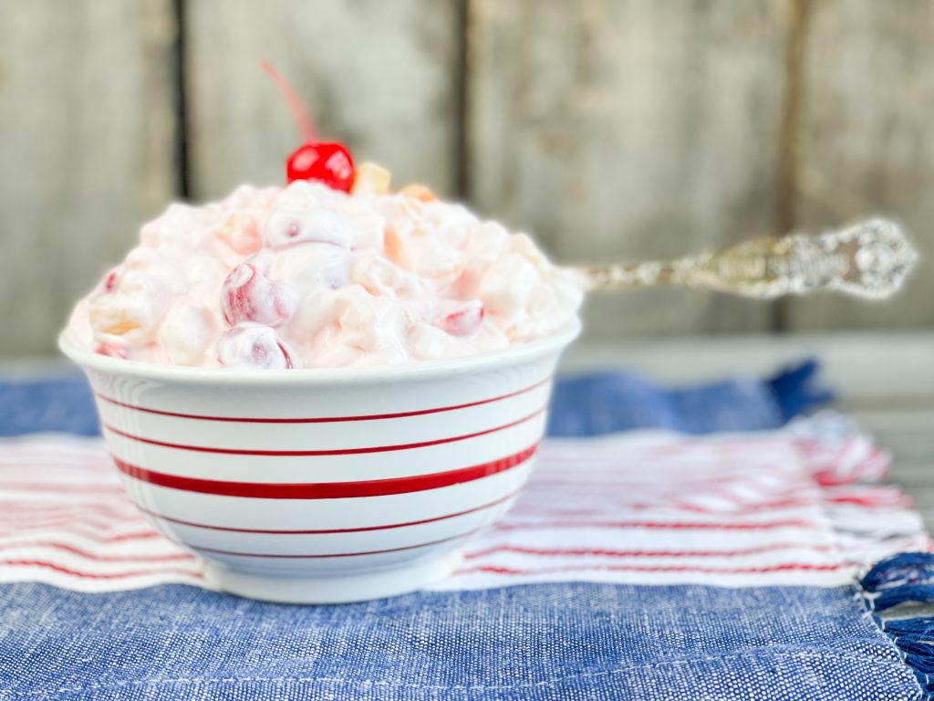 white creamy fruit salad in a bowl with a red cherry on top