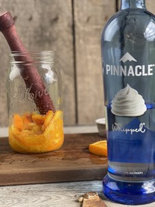 A glass of sugar and orange slices being muddled with a bottle Pinnacle Whipped Cream Vodka for an Orange Shake-up