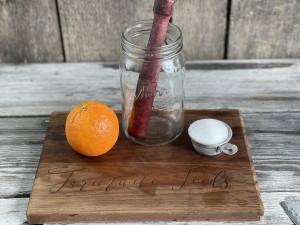 A whole orange, mason jar with muddle and a cup of sugar on a wooden board to make Orange Shake-ups