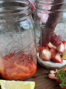 mason jar with lemon and strawberry pieces being muddled in sugar