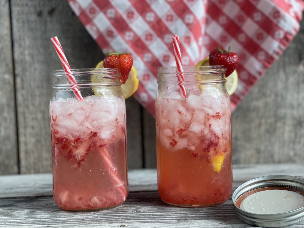 2 mason jars with ice, strawberries and lemon slices with straws