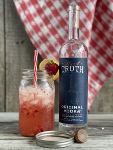 mason jar with ice and strawberry lemonade with a straw and a bottle of Hard Truth Vodka