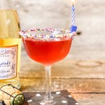 martini glass with red cocktail colorful sprinkles on rim with a birthday candle