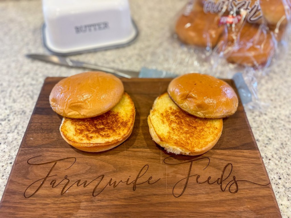 Two lightly toasted brioche buns on a wooden cutting board