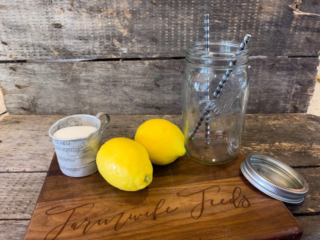 Two whole lemons, measuring cup of sugar and an empty quart jar on a wooden cutting board
