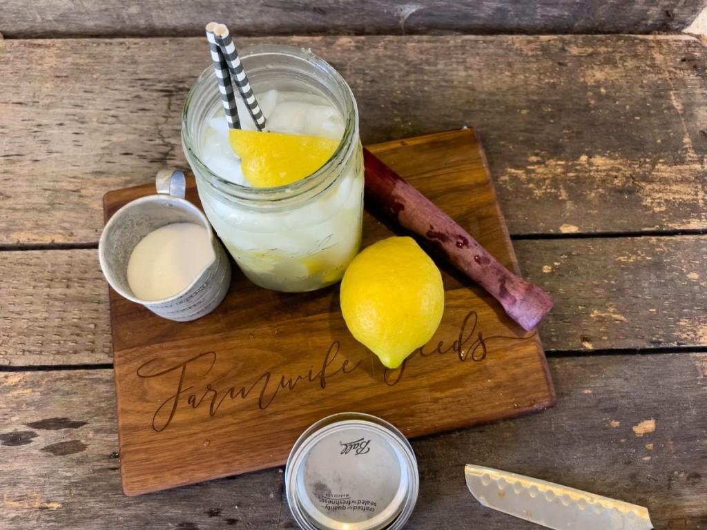 A quart ball jar full of lemon shake up with a whole lemon , a measuring cup of sugar on a wood cutting board