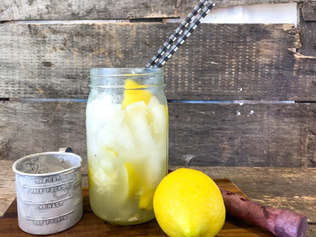 A quart ball jar full of lemon shake up with a whole lemon , a measuring cup of sugar on a wood cutting board