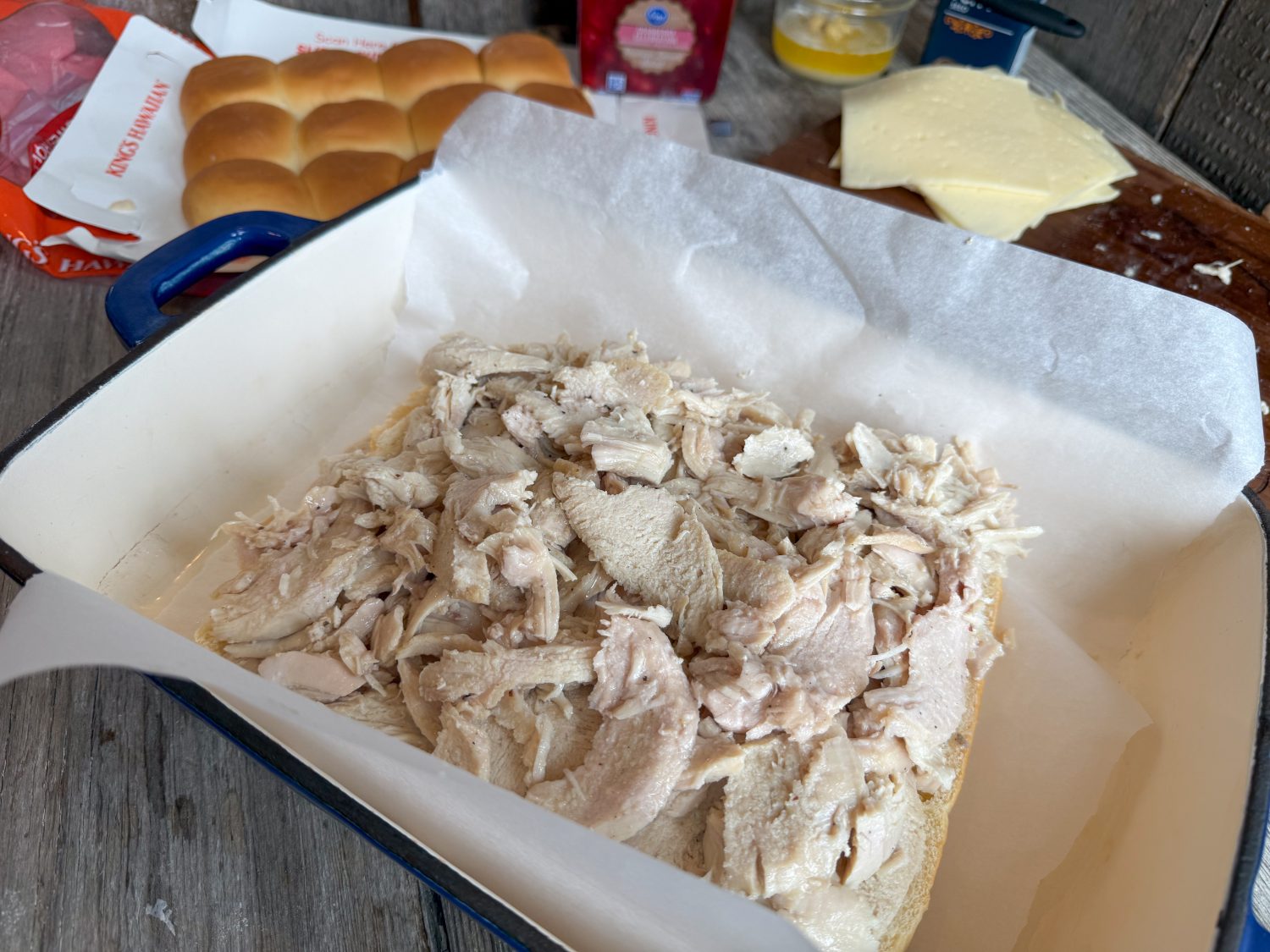 Shredded turkey layered over Hawaiian roll bottoms in a baking dish, ready for assembly into sliders.