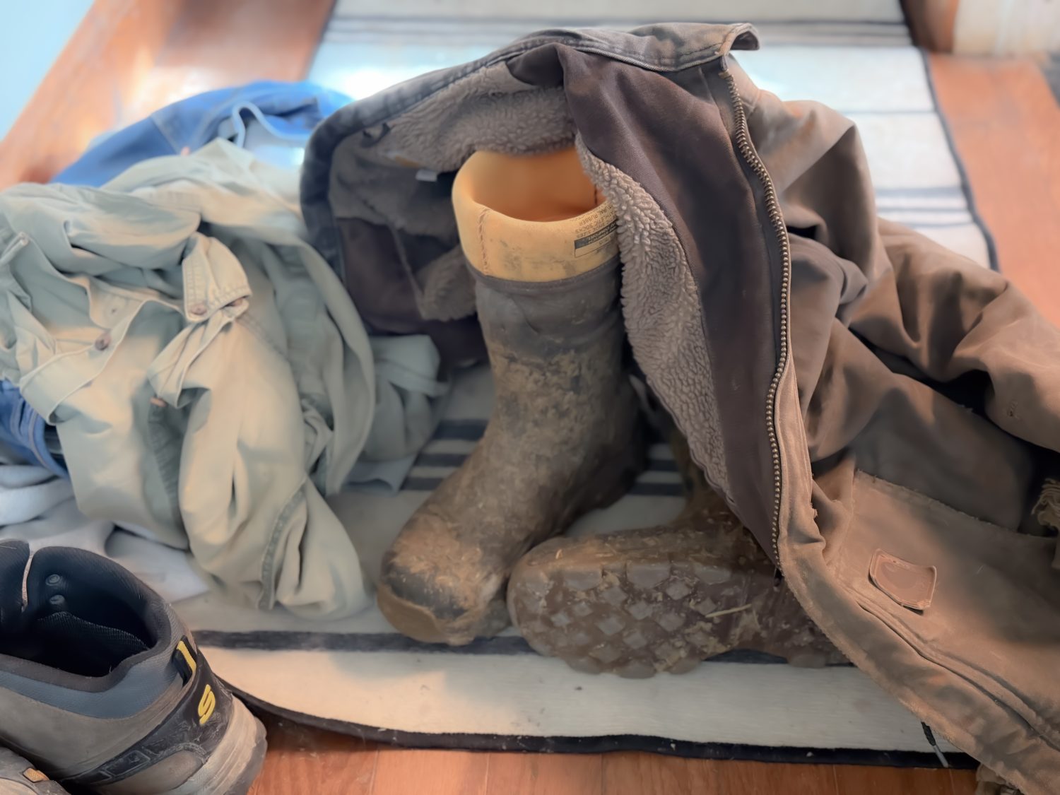 Muddy boots and a torn Carhartt jacket sitting my a kitchen chair, showing the exhaustion and chaos of farm mom life during harvest.
