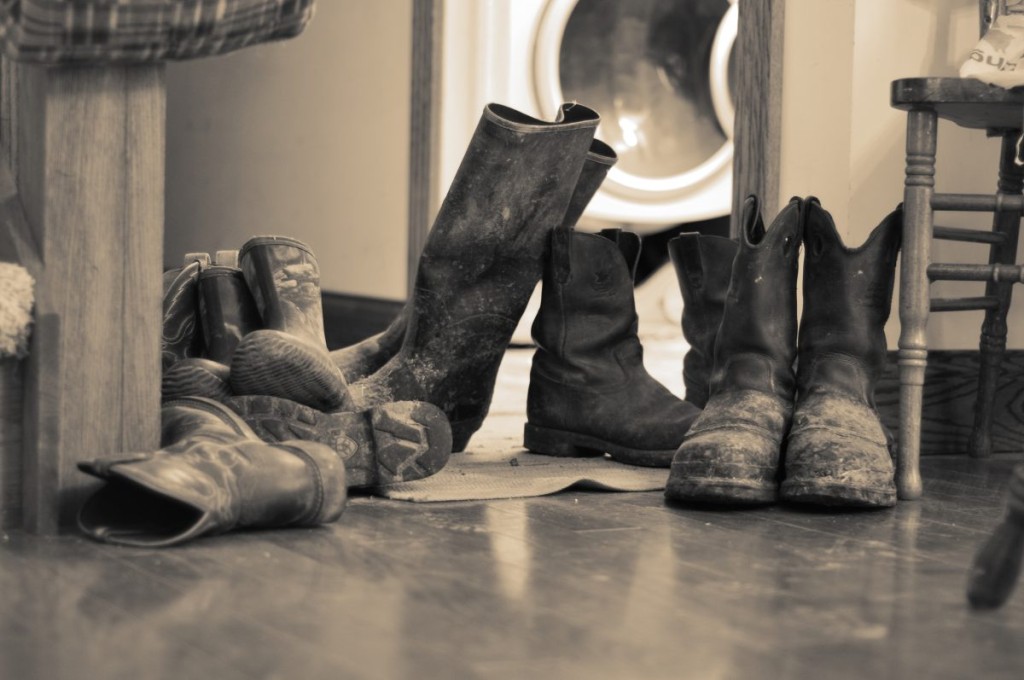 A group of well-worn muddy work botts lined up near a washer and dryer, capturing the daily grit of farm life.