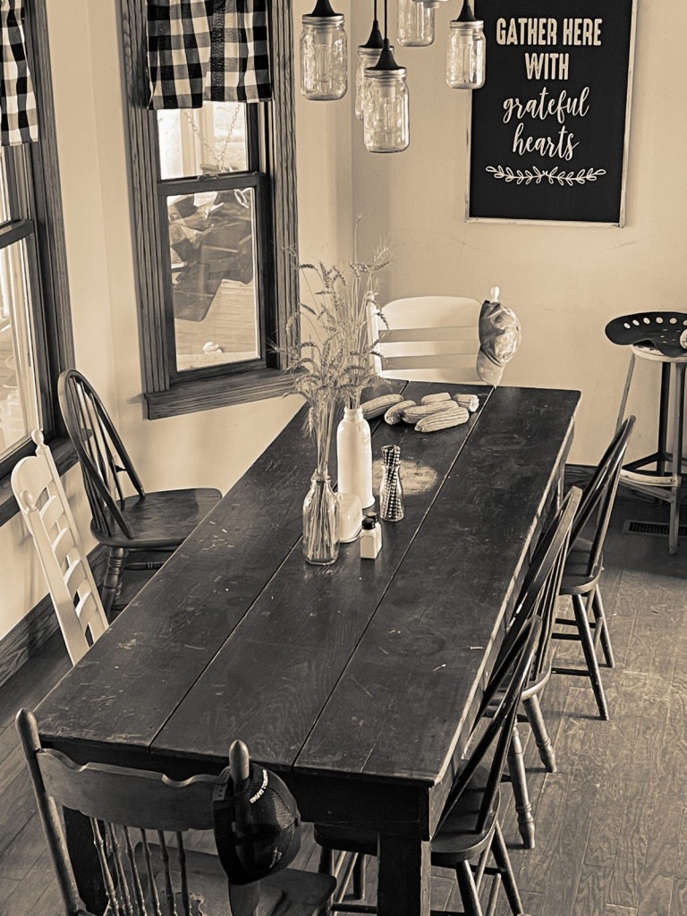 Farmhouse kitchen table set for family gatherings, surrounded by =vintage chairs, mason jar lighting, and a "Gather Here With Grateful Hearts" sign - capturing everyday moments and traditions of farm life storytelling.