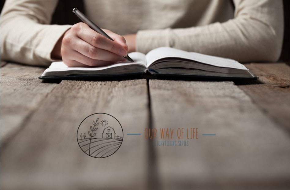 Person writing in an open notebook on a rustic wooden table, symbolizing storytelling for the Our Way of Life series
