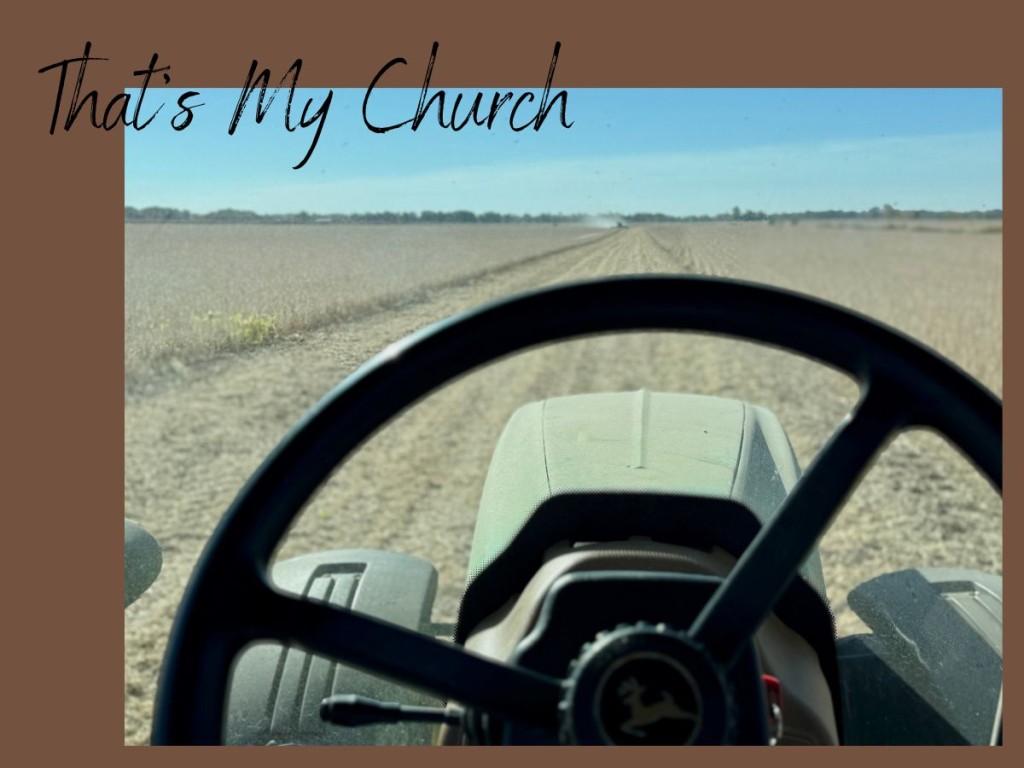 View from inside a John Deere tractor cab during harvest in Indiana, looking across rows of farmland under a clear blue sky — a farmer’s quiet place of reflection and prayer.
