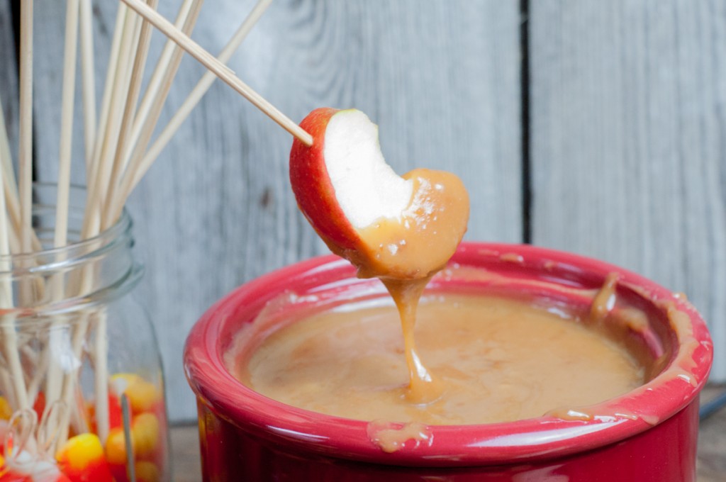 Apple slice on skewer being dipped into warm caramel in a red crockpot.