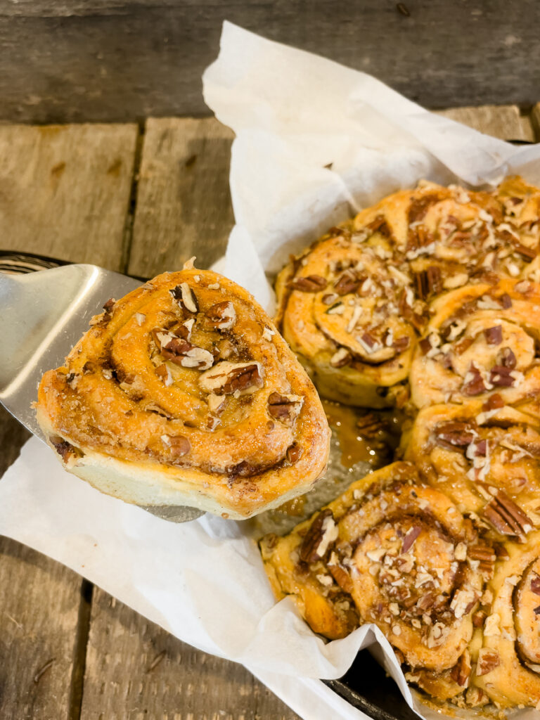 Serving a gooey TikTok Cinnamon Roll from a cast iron skillet with pecans