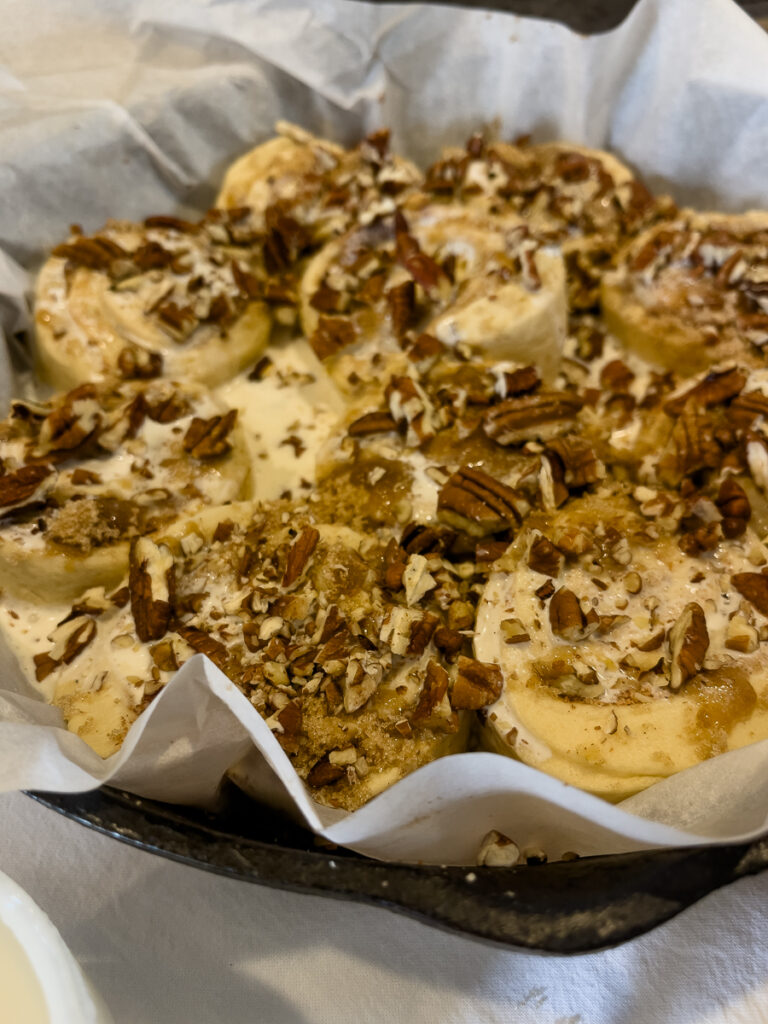Close up of cinnamon rolls topped with brown sugar and pecans in a cast iron skillet before baking